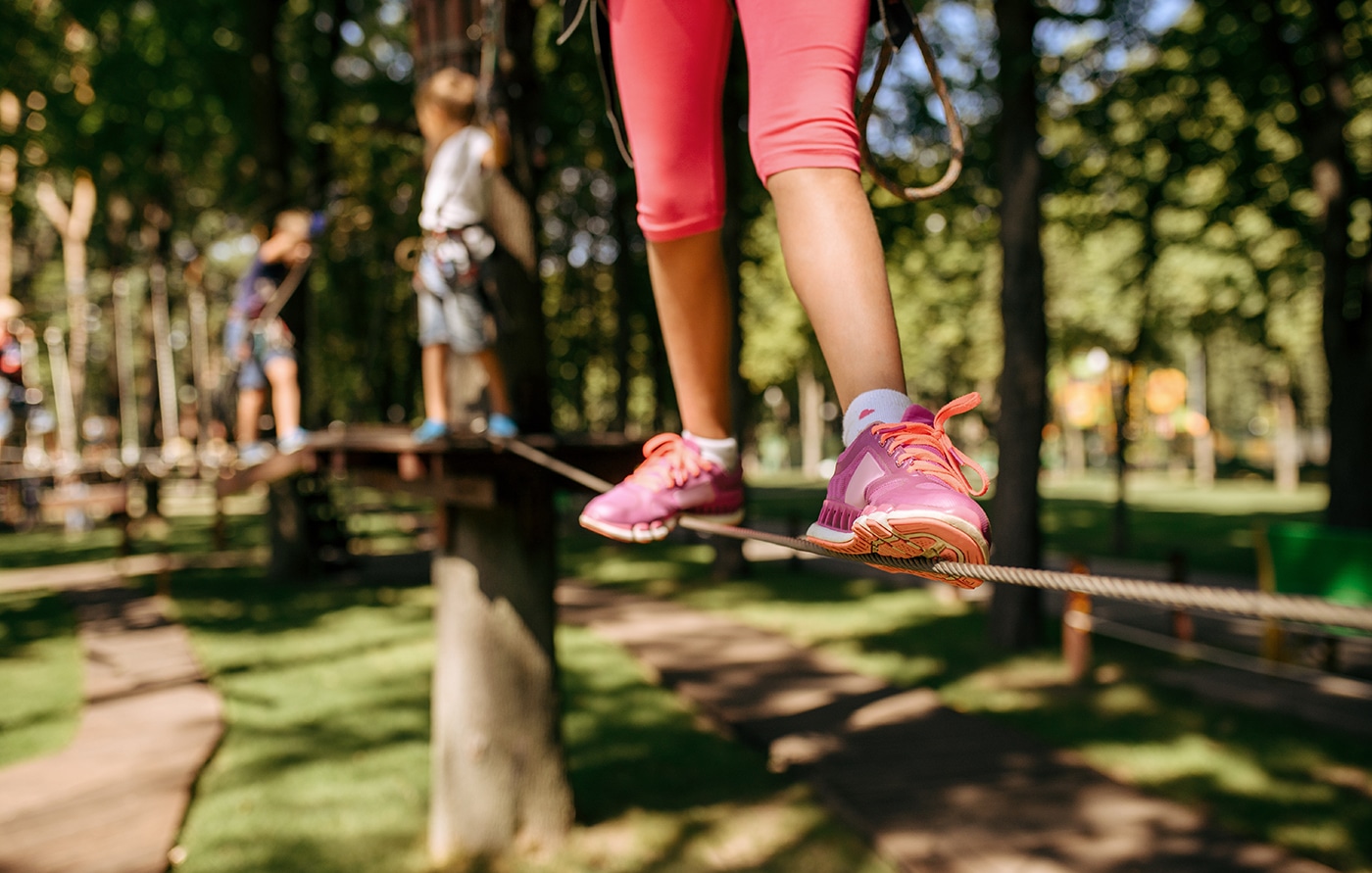 Jente med rosa joggesko går på slakk line i skogen.