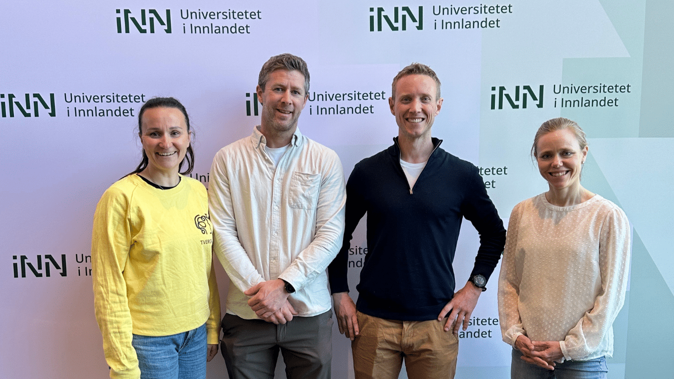 To kvinner og to menn poserer foran en fotovegg, dekorert med logoene til Universitetet i Innlandet.